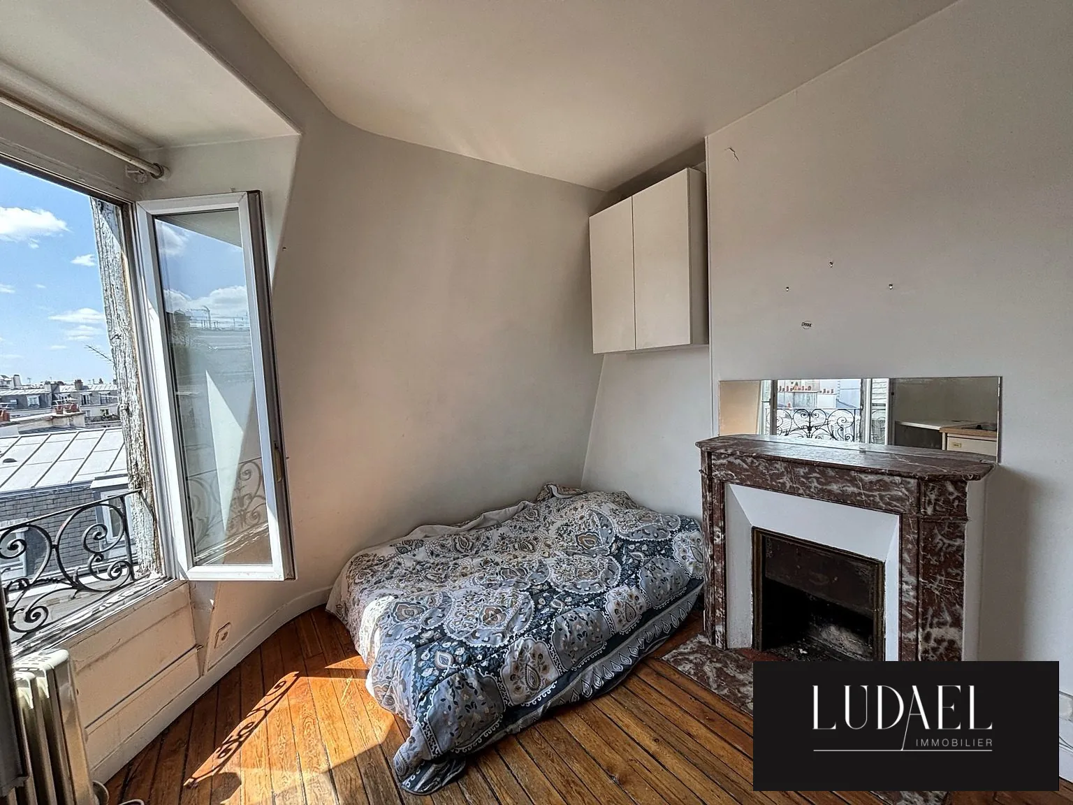 Pièce principale baignée de lumière avec parquet ancien et cheminée Studio avec vue dégagée dans le quartier recherché des Batignolles à Paris